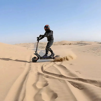 Izdelek na sliki je električni skiro, model Kukirin G2 Master. Vidimo voznika, oblečenega v zaščitno opremo, ki se vozi po peščeni pokrajini. Skuter se premika hitro, kar povzroča prah in pesek, ki se dviga okoli njega. V ozadju so peščene sipine in modro nebo, kar ustvarja dinamično in pustolovsko vzdušje.