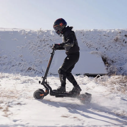 Izdelek na sliki je električni skiro znamke Kukirin, model G2 Master. Na sliki je vidna oseba, ki vozi skiro po zasneženi površini, oblečena v zaščitno opremo, vključno s čelado in zaščitnimi blazinicami. Okolica je prekrita s snegom, kar kaže na zimske razmere.