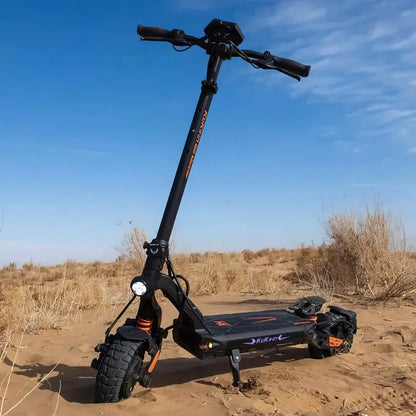 Na sliki je električni skiro, model Kukirin G2 Master. Izdelek ima robustno zasnovo z širokimi pnevmatikami, kar omogoča vožnjo po različnih terenih. Vidna je tudi krmilna enota z ročaji in svetilka na sprednjem delu skiroja. Ozadje prikazuje peščeno okolje z nekaj rastlinjem, kar nakazuje, da je skiro primeren za vožnjo tudi v naravi.