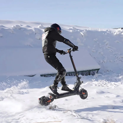 Na sliki je električni skiro znamke Kukirin, model G2 Master. Prikazuje voznika, ki se vozi po snegu, oblečenega v zaščitno opremo, vključno s čelado. Snežna pokrajina in dinamična pozicija voznika nakazujeta na športno in avanturistično uporabo skiroja.