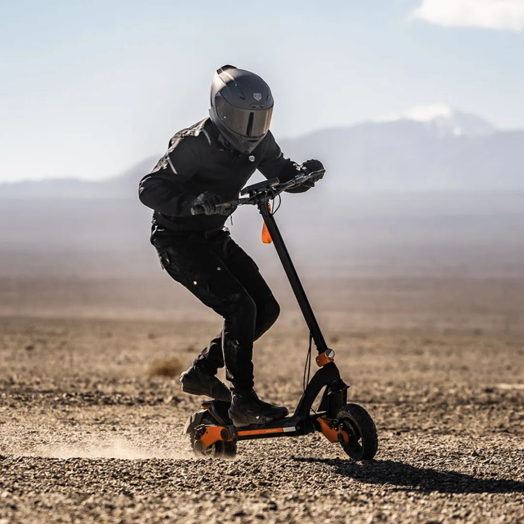 Jezdec s čelado izvaja trike na električnem skiroju Kukirin G3 v puščavski pokrajini.