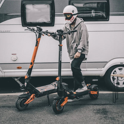 Oseba s čelado stoji ob dveh električnih skirojih Kukirin G3 Pro.