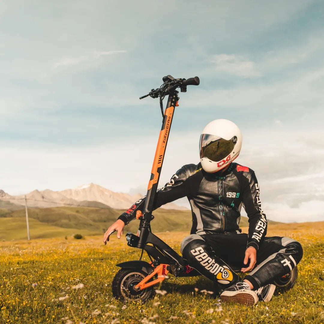 Jezdec s čelado sedi poleg električnega skiroja Kukirin G3 Pro na travnatem polju.