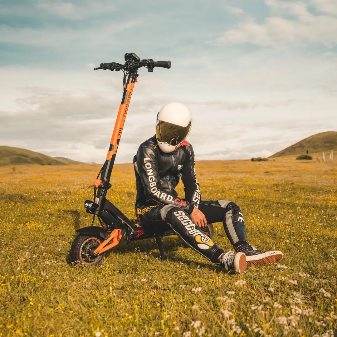 Voznik s čelado sedi ob električnem skiroju Kukirin G3 Pro na travnatem polju.