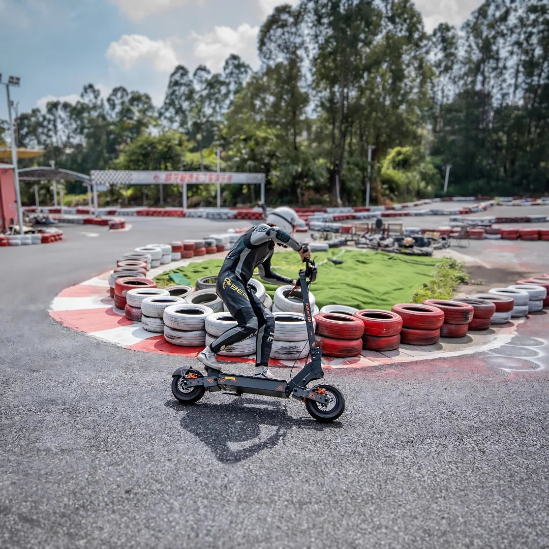 Na sliki je prikazan električni skiro, model Kukirin G4. Na skiroju je oseba v zaščitni opremi, ki se vozi po dirkališču ob robu, obdanim s pnevmatikami. Ozadje prikazuje zeleno območje in druge elemente dirkališča, kar daje občutek dinamike in hitrosti.