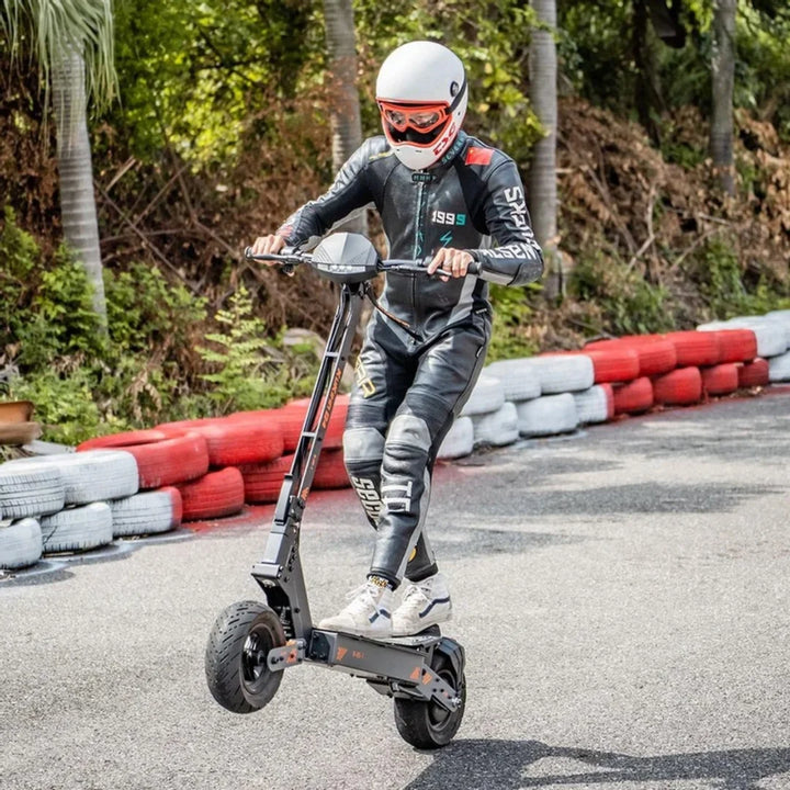 Voznik v dirkalni obleki izvaja trike na električnem skiroju Kukirin G4 na stezi.