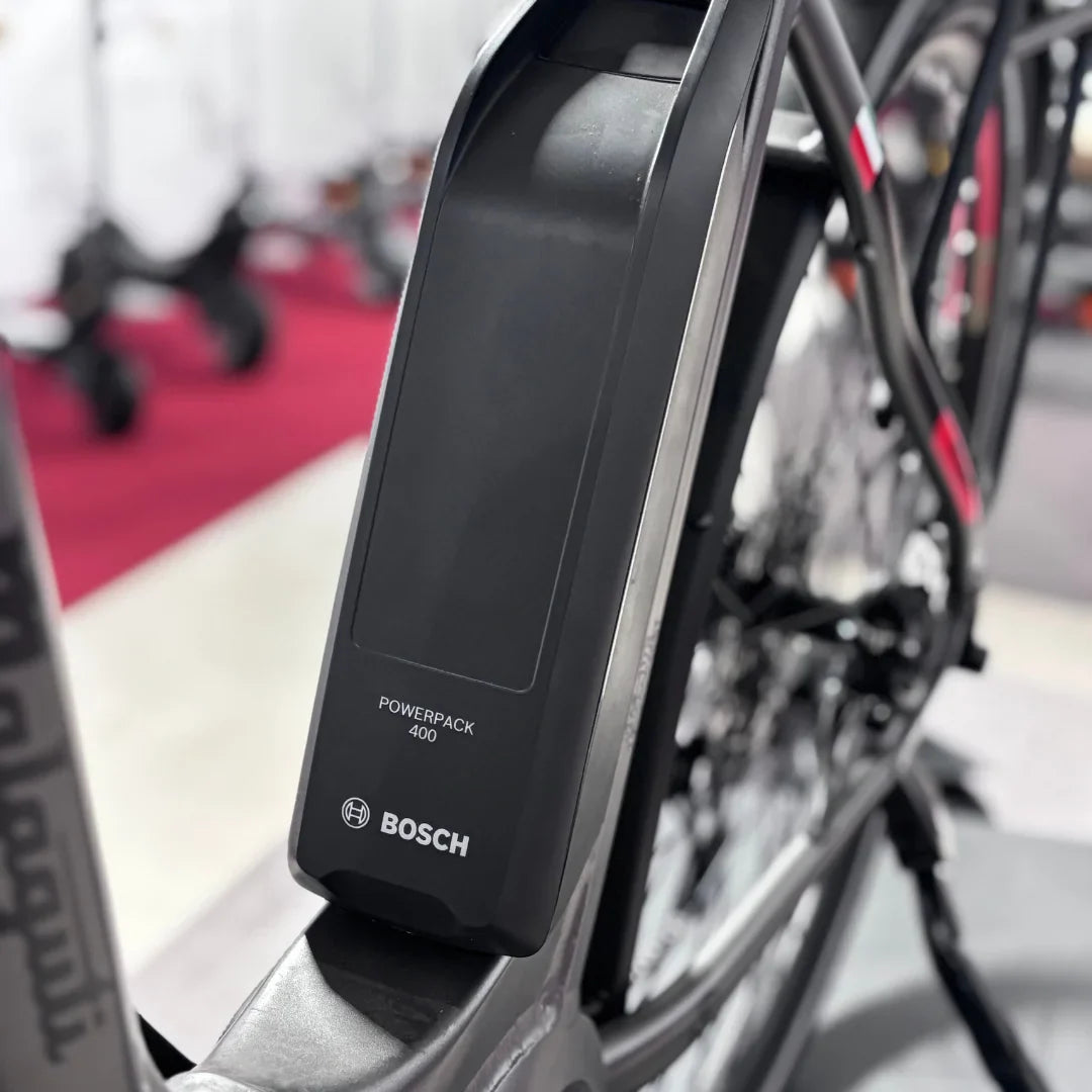 Izdelek na sliki je električno kolo znamke Malaguti, model Bolonina. Na sliki je prikazana baterija Bosch Powerpack 400, ki je nameščena na okvirju kolesa. Oprema kolesa nakazuje na sodobno zasnovo in tehnologijo, kar je značilno za električna kolesa. V ozadju so vidni tudi drugi kolesi, kar kaže na okolje, kjer je izdelek razstavljen.