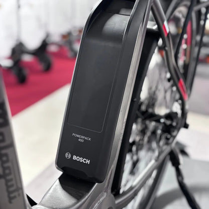 Izdelek na sliki je električno kolo znamke Malaguti, model Bolonina. Na sliki je prikazana baterija Bosch Powerpack 400, ki je nameščena na okvirju kolesa. Oprema kolesa nakazuje na sodobno zasnovo in tehnologijo, kar je značilno za električna kolesa. V ozadju so vidni tudi drugi kolesi, kar kaže na okolje, kjer je izdelek razstavljen.