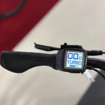 Na sliki je prikaz električnega kolesa znamke Malaguti, model Bolonina. Vidna je krmilo s prikazovalnikom, ki prikazuje hitrost in način vožnje (Turbo). Prikazovalnik ima gumbe za prilagajanje hitrosti in načinov, kar omogoča enostavno upravljanje med vožnjo.