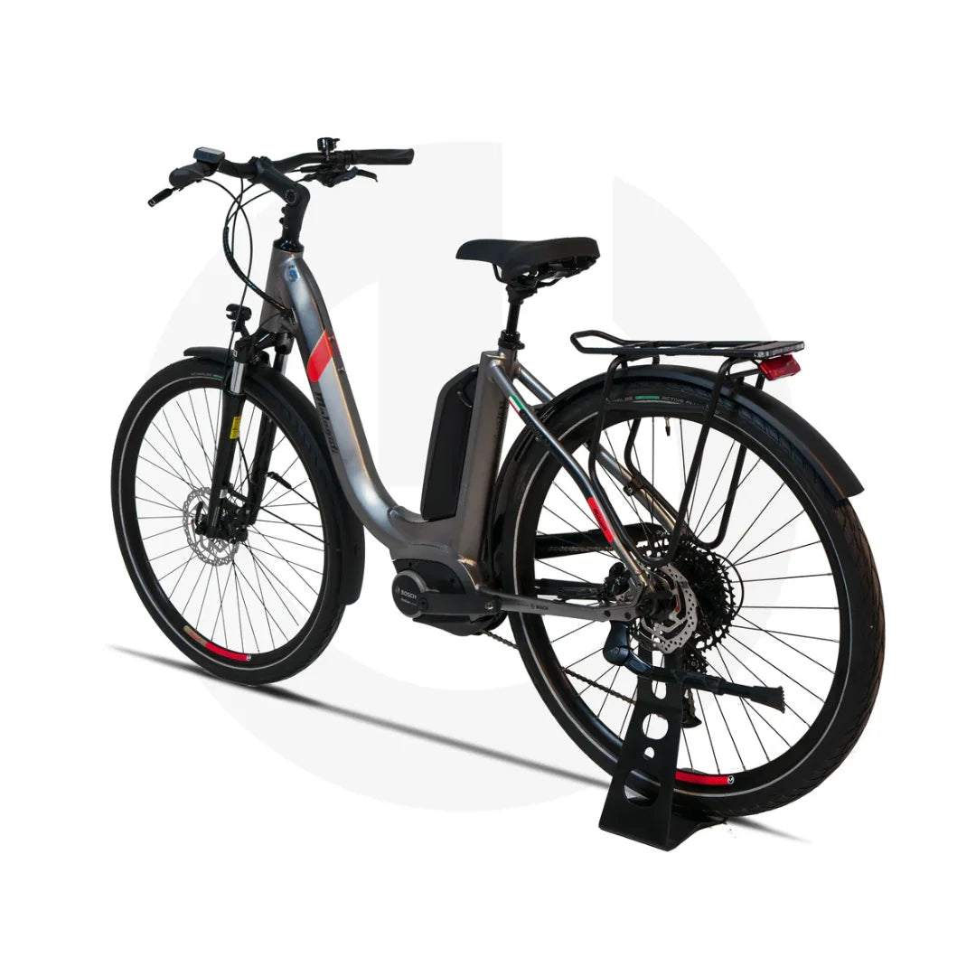 Na sliki je električno kolo znamke Malaguti, model Bolonina. Kolo ima moderno obliko s sredinskim motorjem in baterijo, ki je nameščena na okvirju. Vidni so tudi široki kolesi, disk zavore ter nosilec za prtljago na zadnjem delu. Barvna kombinacija vključuje srebrno in črne odtenke, kar daje kolesu eleganten videz.