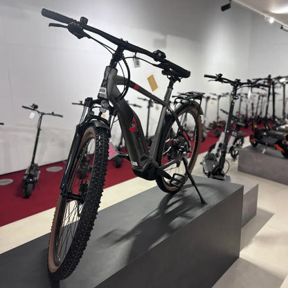 Na sliki je električno kolo znamke Malaguti, model Carezza TR 4.0 v visokem koraku. Kolo ima robusten okvir, široke gume z grobim profilom, kar omogoča dobro oprijemljivost na različnih terenih. V ozadju so vidni tudi električni skiroji, kar nakazuje, da gre za prodajno mesto, specializirano za električna prevozna sredstva.