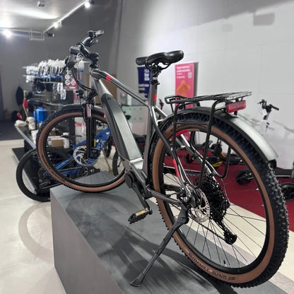 Izdelek na sliki je električno kolo znamke Malaguti, model Carezza TR 4.0 z visokim korakom. Kolo ima moderno zasnovo, opremljeno z električnim motorjem in baterijo, kar omogoča enostavno in udobno vožnjo. Na sliki je vidna tudi zadnja prtljažna mreža ter široki kolesi z gumami, ki so primerne za različne terene. V ozadju so vidni drugi kolesi in oprema, kar nakazuje, da gre za prodajno mesto ali servis.