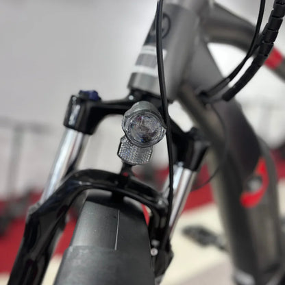 Izdelek je električno kolo, znamke Malaguti, model Carezza TR 4.0 High Step. Na sliki je vidna prednja luč, ki je nameščena na vilicah kolesa, ter del okvirja in krmila. Kolo ima sodoben dizajn in je primerno za različne terene.