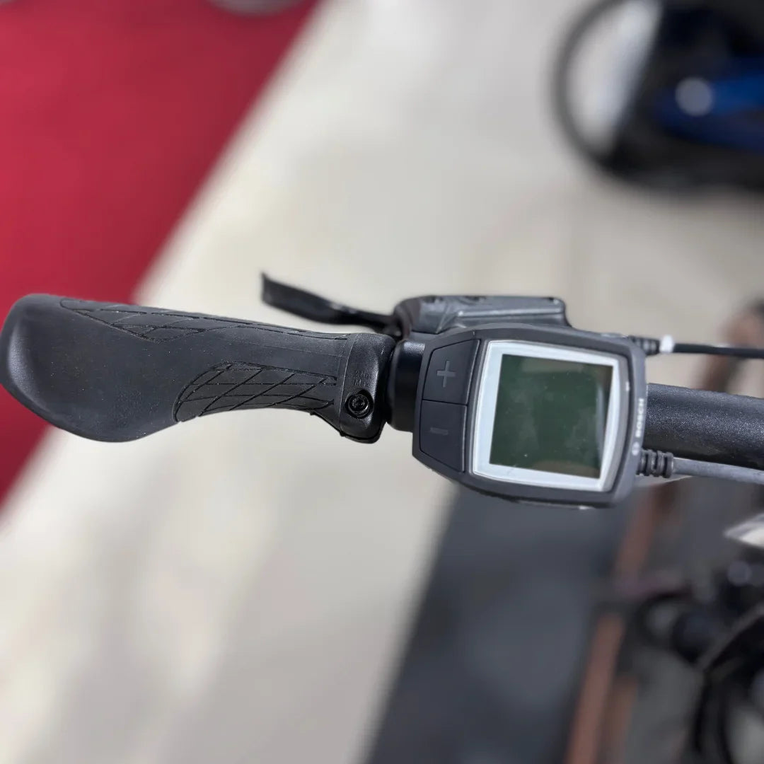 Izdelek je električno kolo znamke Malaguti, model Carezza TR 4.0 High Step. Na sliki je prikazan del krmila, ki vključuje ročaj in zaslon za upravljanje, ki omogoča nastavitev različnih funkcij kolesa. Ročaj je oblikovan za udoben oprijem, zaslon pa prikazuje informacije o delovanju kolesa.