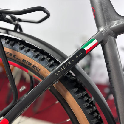 Izdelek na sliki je električno kolo, znamke Malaguti, model Carezza TR 4.0. Na sliki je vidna zadnja cev okvirja, na kateri je označen model "Carezza 4.0". Kolo ima široke gume s profilom, ki je primeren za različne terene, ter značilno barvno kombinacijo, ki vključuje italijansko zastavo.