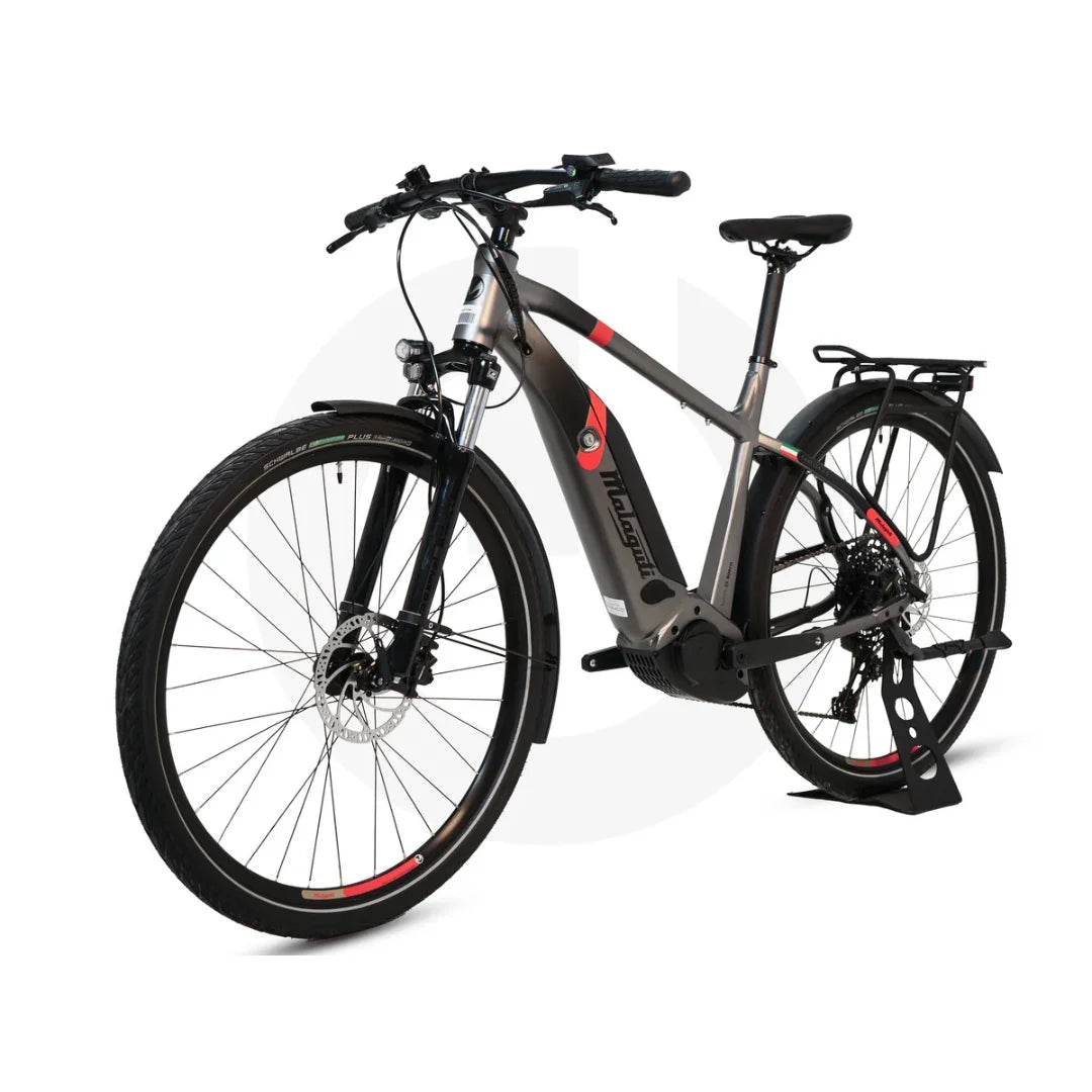 Izdelek na sliki je električno kolo znamke Malaguti, model Carezza TR 4.0 High Step. Kolo ima robustno zasnovo z močnim okvirjem, širokimi pnevmatikami ter disk zavorami, kar omogoča dobro stabilnost in nadzor pri vožnji. Vidni so tudi dodatki, kot so nosilec za prtljago in sprednje luči, kar kaže na njegovo uporabnost za mestno in rekreativno vožnjo.