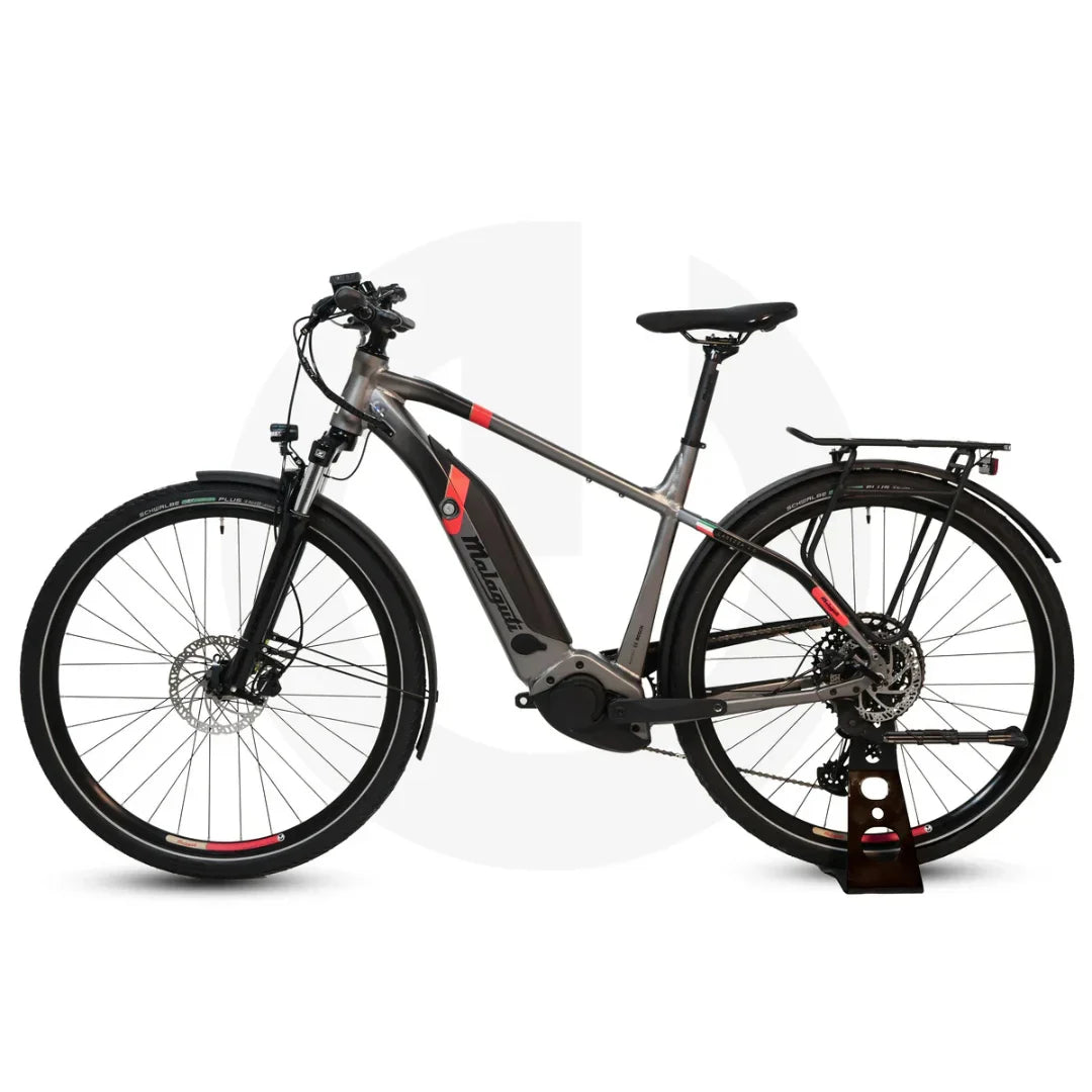 Izdelek na sliki je električno kolo znamke Malaguti, model Carezza TR 4.0 High Step. Kolo ima robustno zasnovo z močnim okvirjem, električni motor in disk zavore, kar omogoča udobno in varno vožnjo. Vidna sta tudi nosilec za prtljago in široka kolesa, kar dodatno povečuje funkcionalnost in stabilnost pri vožnji.