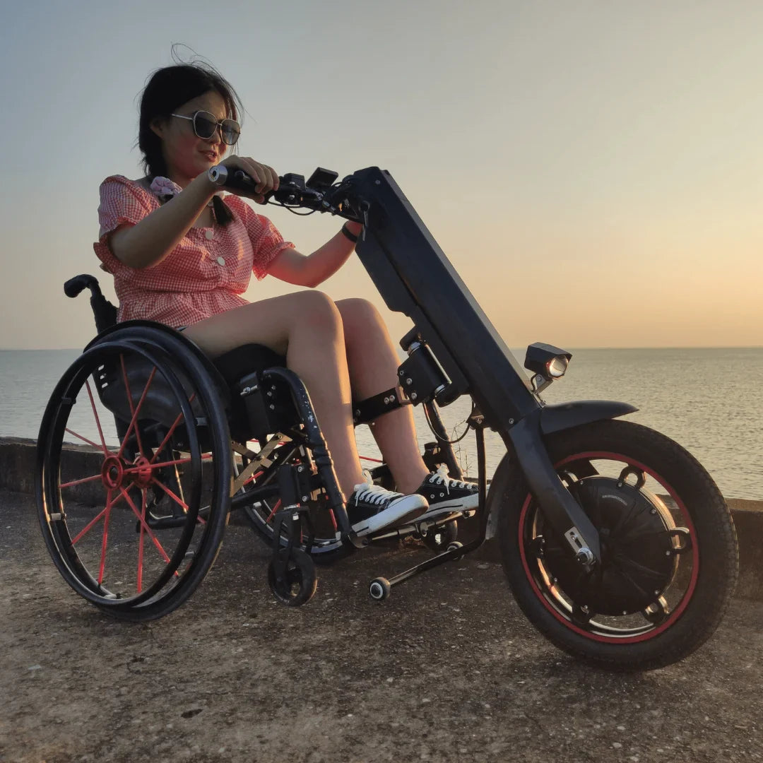 Izdelek na sliki je električni priklop za invalidski voziček, model Mijo MT03. Na sliki je vidna oseba, ki uporablja ta priklop, kar omogoča enostavno premikanje s pomočjo električnega motorja. Priklop je zasnovan tako, da se prilega invalidskemu vozičku, kar povečuje mobilnost uporabnika. V ozadju je vidna obala ob sončnem zahodu, kar dodaja prijeten ambient.