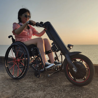 Izdelek na sliki je električni priklop za invalidski voziček, model Mijo MT03. Na sliki je vidna oseba, ki uporablja ta priklop, kar omogoča enostavno premikanje s pomočjo električnega motorja. Priklop je zasnovan tako, da se prilega invalidskemu vozičku, kar povečuje mobilnost uporabnika. V ozadju je vidna obala ob sončnem zahodu, kar dodaja prijeten ambient.