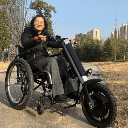 Izdelek na sliki je električni priklop za invalidski voziček, model Mijo MT03. Na sliki je oseba, ki sedi v invalidskem vozičku, opremljenem z električnim priklopom. Ta naprava omogoča enostavno premikanje in mobilnost, saj je zasnovana za pomoč uporabnikom invalidskih vozičkov pri premikanju. Oseba se z veseljem vozi po poti v parku, kar kaže na udobje in funkcionalnost izdelka.