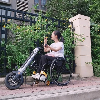 Izdelek na sliki je električni priklop za invalidski voziček, model Mijo MT03. Na sliki je vidna ženska, ki sedi v invalidskem vozičku, opremljenem z električnim priklopom, kar omogoča enostavno premikanje. Okoli nje so rastline, kar daje prijeten občutek narave. Priklop je zasnovan za izboljšanje mobilnosti uporabnikov invalidskih vozičkov.