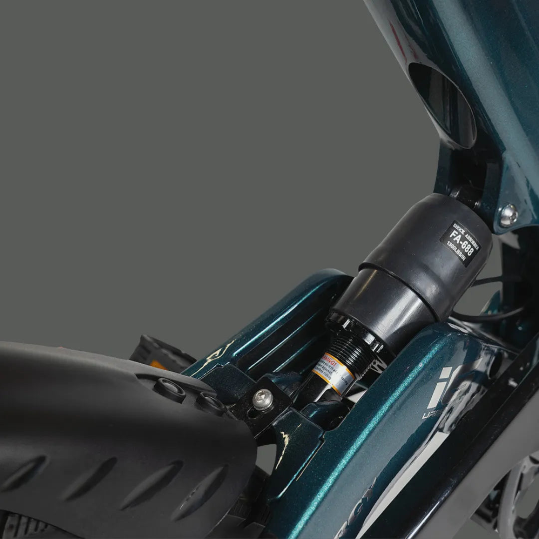 Izdelek na sliki je električno kolo, model MS Energy Urbanfold i6. Na sliki je vidna podrobnost okvirja kolesa, ki je v temno zeleni barvi, ter amortizer, kar nakazuje na udobno vožnjo. Kolo ima zložljivo zasnovo, kar omogoča enostavno shranjevanje in prenašanje.