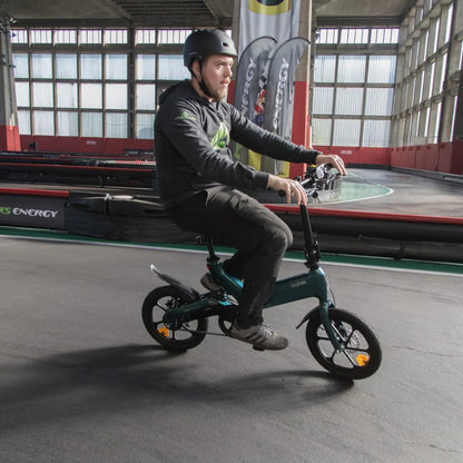 Izdelek na sliki je električno kolo, znamke MS Energy, model Urbanfold i6. Na sliki je moški, ki vozi električno kolo na zaprtem prostoru, obdanem z različnimi zastavami in rdečimi stenami. Kolo ima majhne kolesa in kompaktno zasnovo, kar ga dela primerno za mestno vožnjo. Opremljeno je z zaščitno čelado, kar nakazuje na varno uporabo.