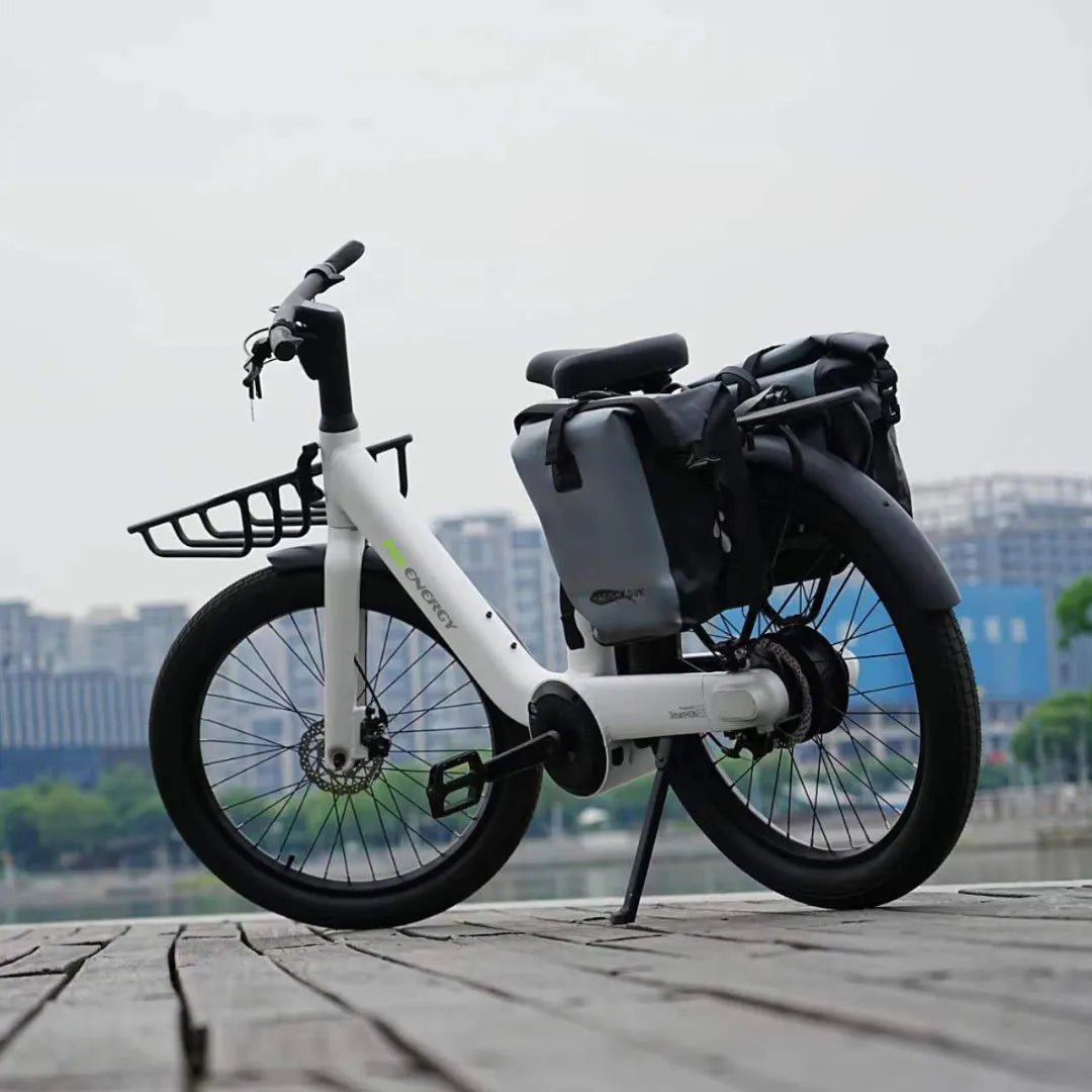 Belo električno kolo Ms Energy Cityzen C102 parkirano ob obali, z mestno panoramo v ozadju