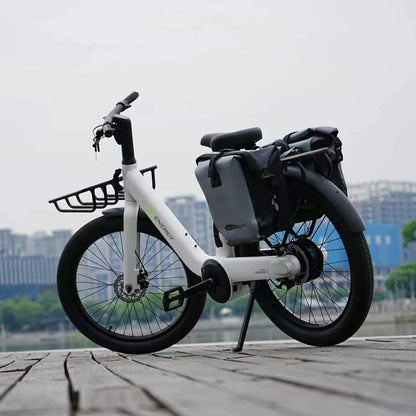 Belo električno kolo Ms Energy Cityzen C102 parkirano ob obali, z mestno panoramo v ozadju