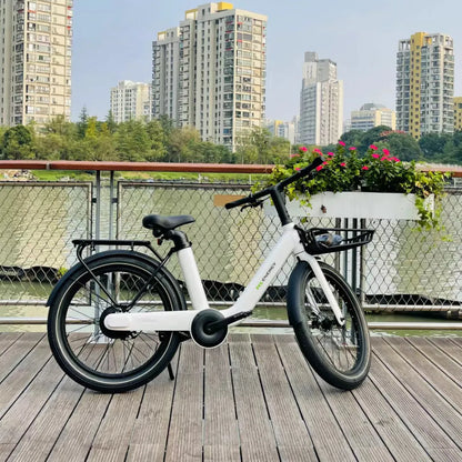 Izdelek na sliki je električno kolo, model MS Energy Cityzen C102. Kolo je belo, ima udoben sedež in široke pnevmatike, kar zagotavlja stabilnost in udobno vožnjo. Na sliki je kolo postavljeno na leseno ploščad ob vodi, v ozadju pa so vidne moderne zgradbe in cvetlična zasaditev.