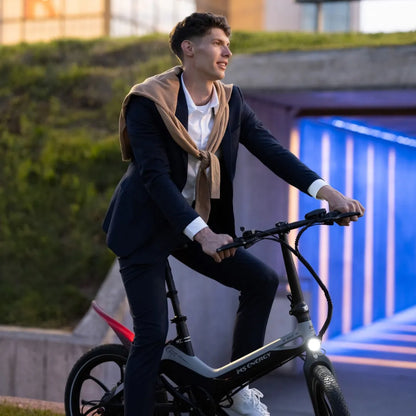 Izdelek na sliki je električno kolo, model MS Energy I20. Na sliki je moški v poslovnem obleku, ki se vozi na kolesu. Kolo ima moderno zasnovo in je opremljeno z lučjo spredaj. V ozadju je arhitekturna struktura, ki ustvarja sodoben ambient.