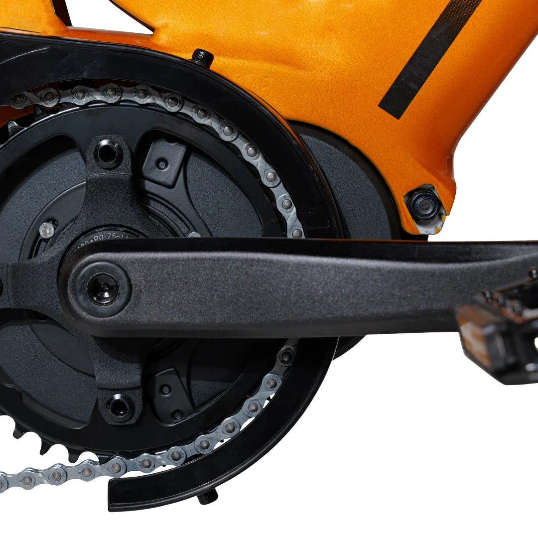 Izdelek je električno kolo, model MS Energy SUV C502. Na sliki je prikazan del pogonskega sistema, ki vključuje verigo in pedalni sistem. Barva okvirja je oranžna, kar daje kolesu dinamičen videz. Vidni so tudi deli, ki omogočajo povezavo med pedalom in motorjem, kar je ključno za delovanje električnega kolesa.