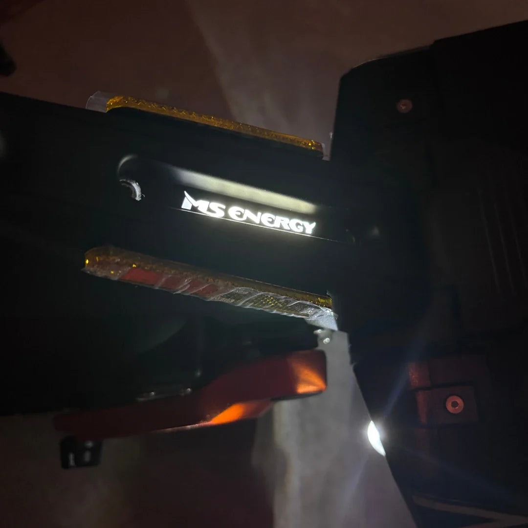 Izdelek na sliki je električni skiro, model MS Energy Flare X Pro. Na sliki je vidna oznaka znamke "MS ENERGY", ki je osvetljena, ter del konstrukcije skiroja, ki vključuje reflektorje in mehanizem za zlaganje. Skupna zasnova nakazuje na robustnost in funkcionalnost, kar je značilno za električne skiroje.