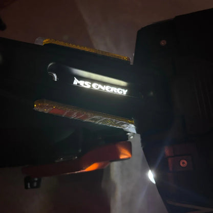 Izdelek na sliki je električni skiro, model MS Energy Flare X Pro. Na sliki je vidna oznaka znamke "MS ENERGY", ki je osvetljena, ter del konstrukcije skiroja, ki vključuje reflektorje in mehanizem za zlaganje. Skupna zasnova nakazuje na robustnost in funkcionalnost, kar je značilno za električne skiroje.