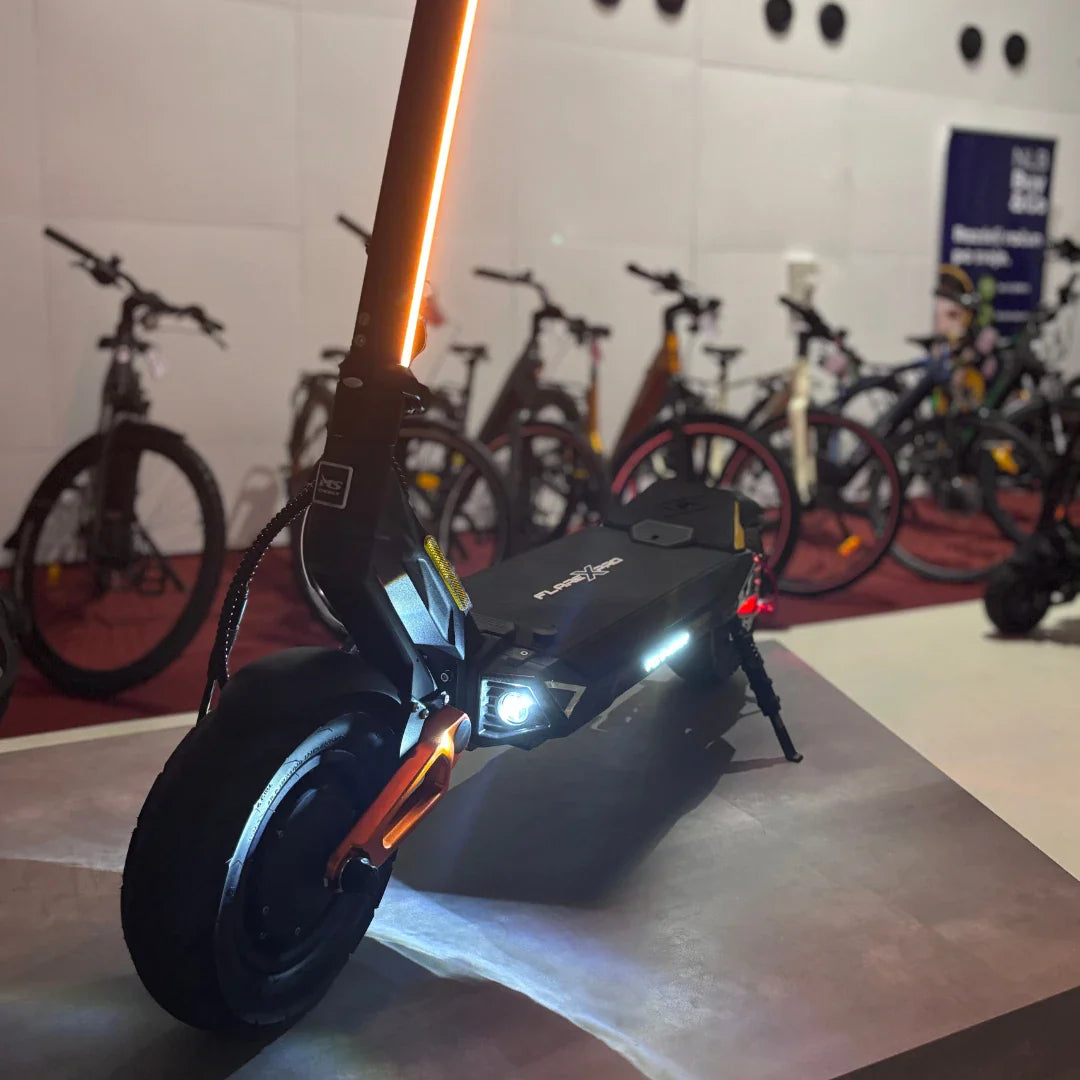 Izdelek na sliki je električni skiro, model MS Energy Flare X Pro. Na sliki je prikazan skiro s sodobnim dizajnom, ki vključuje svetlobne elemente, kot so sprednja lučka in LED trak na ročaju. V ozadju so vidne tudi druge kolesarske naprave, kar nakazuje, da gre za razstavo ali prodajni prostor za električna vozila.