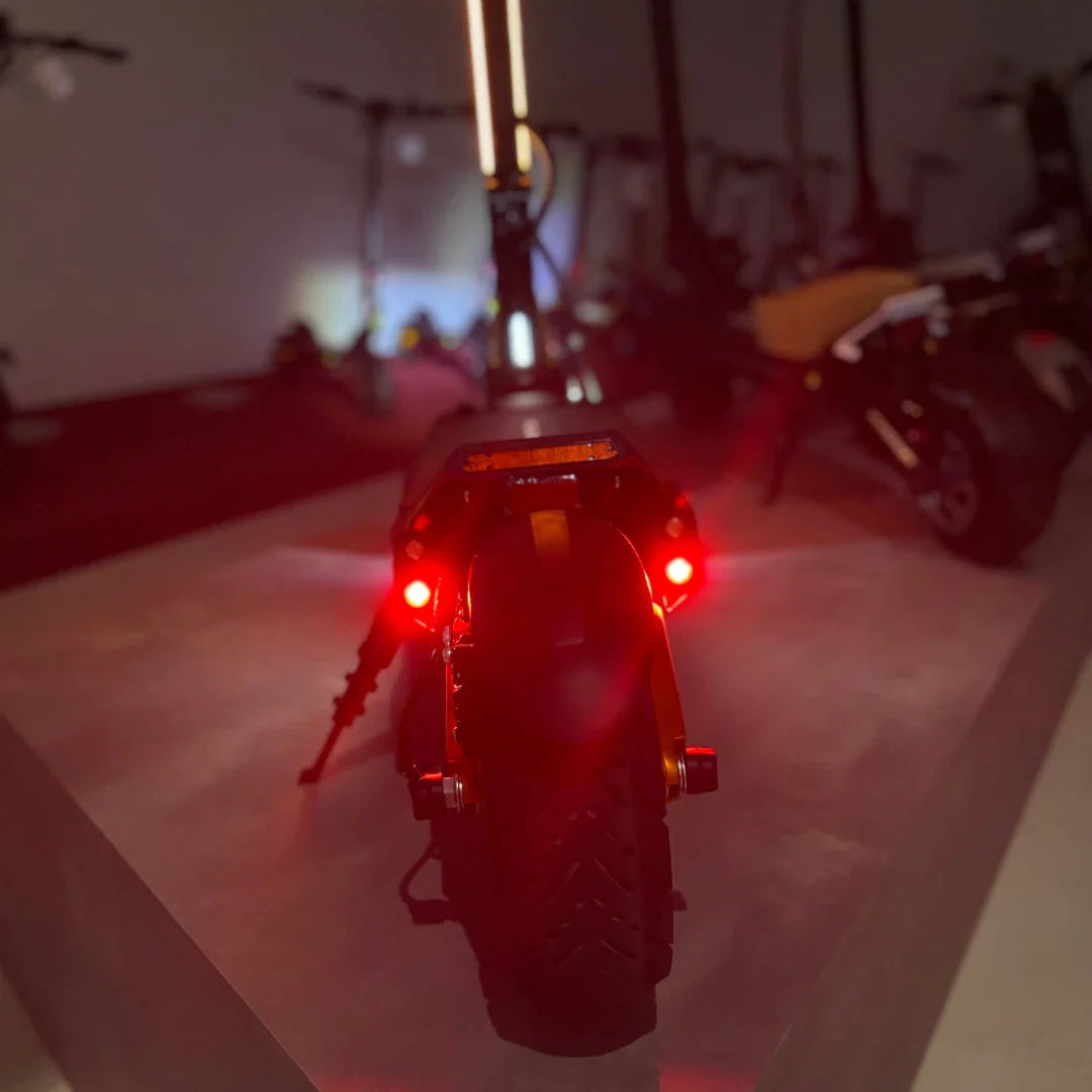 Izdelek na sliki je električni skiro, model MS Energy Flare X Pro. Na sliki je prikazan zadnji del skiroja, ki ima rdeče luči in robustne pnevmatike, kar nakazuje na njegovo zmogljivost in varnost pri vožnji. V ozadju so vidni tudi drugi skiroji, kar ustvarja občutek razstave.