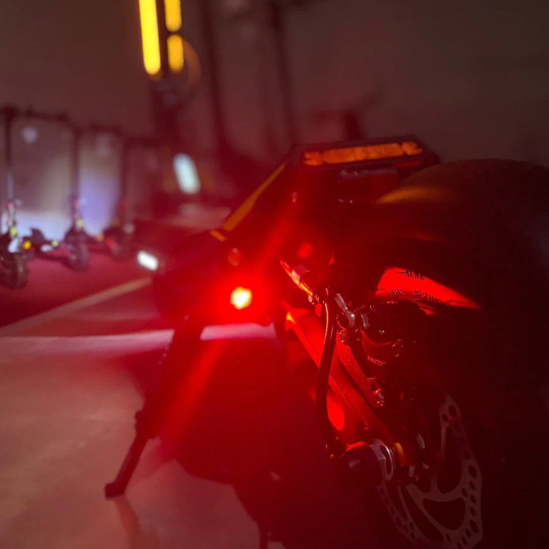 Na sliki je električni skiro, model MS Energy Flare X Pro. Vidna je zadnja stran skiroja, kjer se nahaja rdeča luč, ki zagotavlja vidnost v temi. Opremljen je z močnimi kolesi in zavorami, kar nakazuje na njegovo zmogljivost in varnost pri vožnji. V ozadju so vidni tudi drugi skiroji, kar daje občutek o večji izbiri izdelkov.