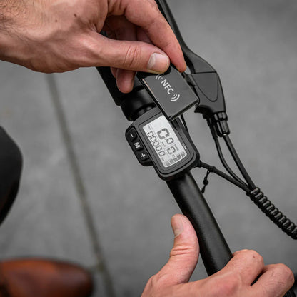 Izdelek je električno kolo znamke MS Energy, model Urbanfold i6. Na sliki je prikazan del krmila, kjer je vidna digitalna naprava, ki prikazuje različne informacije, kot so hitrost in prevožena razdalja. Uporabnik drži NFC napravo blizu zaslona, kar nakazuje na funkcionalnosti, povezane z digitalnim upravljanjem.