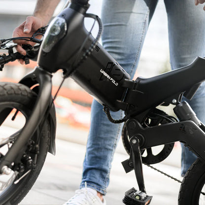 Izdelek na sliki je električno kolo, znamke MS Energy, model UrbanFold i6. Na sliki je prikazana oseba, ki drži kolo, pri čemer je vidna njegova zložljiva konstrukcija, motor ter pedala. Kolo je v črni barvi, kar mu daje sodoben in minimalističen videz.