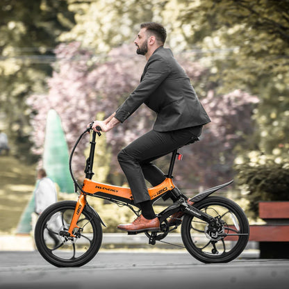 Na sliki je električno kolo znamke MS Energy, model i20. Kolo je v svetlo oranžni barvi in ima kompakten dizajn, kar ga naredi primernega za mestno vožnjo. Na sliki je moški v poslovnem obleku, ki se vozi na kolesu, kar kaže na njegovo praktičnost in uporabnost v urbanem okolju. V ozadju so vidni zeleni drevesi, kar ustvarja prijetno naravno vzdušje.