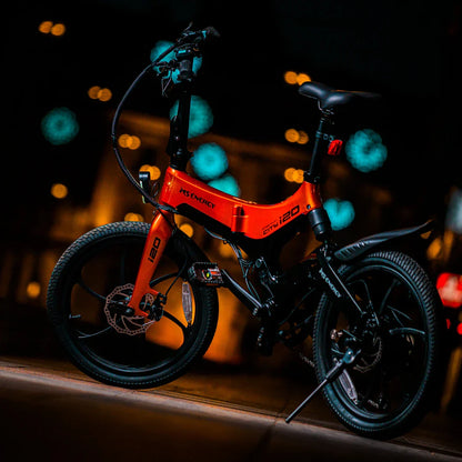 Izdelek na sliki je električno kolo znamke MS Energy, model i20. Kolo ima značilno svetlo oranžno barvo s črnimi detajli in je opremljeno z debelimi pnevmatikami ter modernim dizajnom. Na sliki je kolo postavljeno v nočnem okolju, kar poudarja njegove oblikovne linije in detajle.