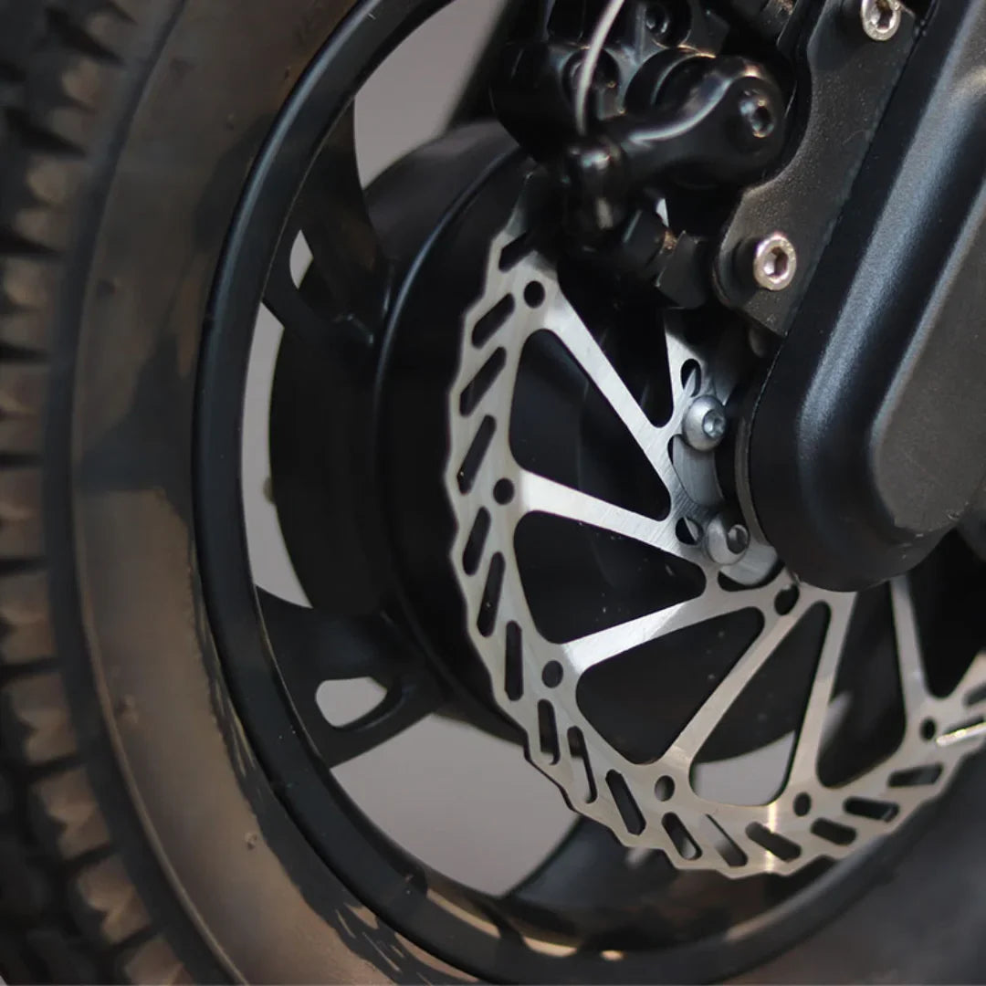 Izdelek je električni skiro, model Mijo MT01. Na sliki je prikazan del kolesa, kjer je vidna disk zavora iz nerjavečega jekla, ki je zasnovana za učinkovito zaviranje. Kolo je obkroženo z gumami, ki zagotavljajo stabilnost in oprijem med vožnjo.