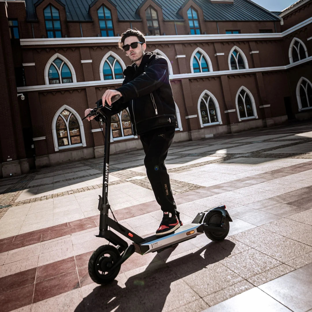 Oseba stoji na električnem skiroju Navee S40 v urbanem okolju z zgodovinsko arhitekturo.