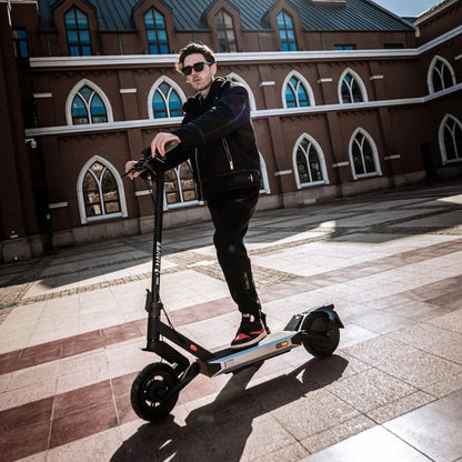 Oseba stoji na električnem skiroju Navee S40 v urbanem okolju z zgodovinsko arhitekturo.