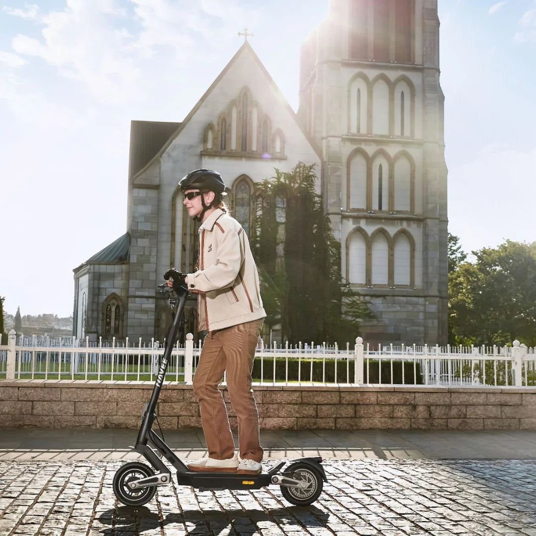 Oseba se vozi z električnim skirojem Navee S40 pred cerkvijo na sončen dan.