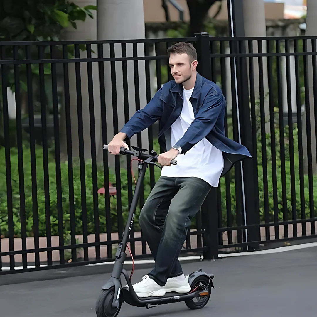 Oseba se vozi z električnim skirojem Navee V40i Pro po gladki površini v bližini zelenja.