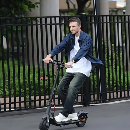 Oseba se vozi z električnim skirojem Navee V40i Pro po gladki površini v bližini zelenja.