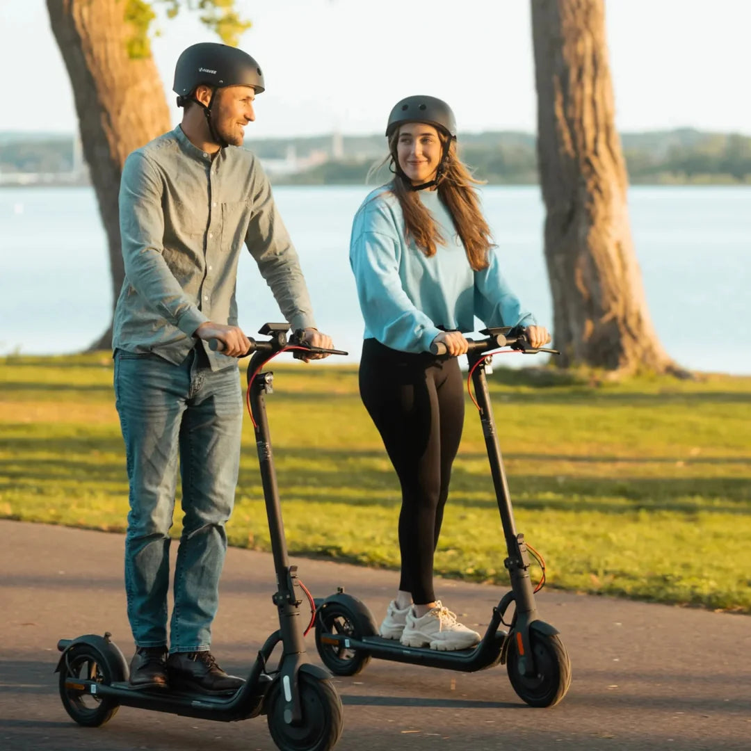 Dve osebi se vozita z električnim skirojem Navee V50i Pro po slikoviti poti ob jezeru.