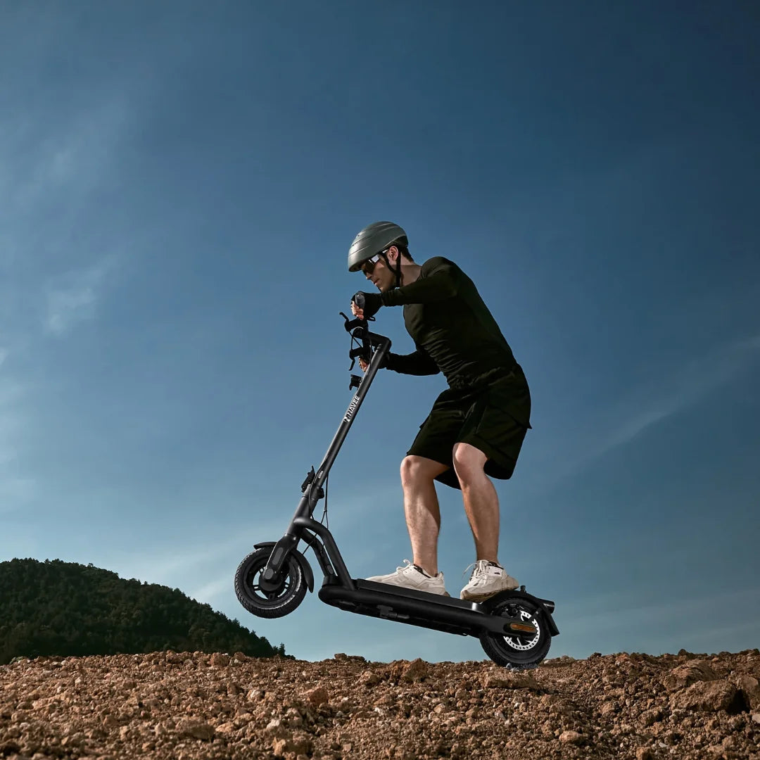 Oseba se vozi z električnim skirojem Navee N65i po skalnatem terenu pod modrim nebom.