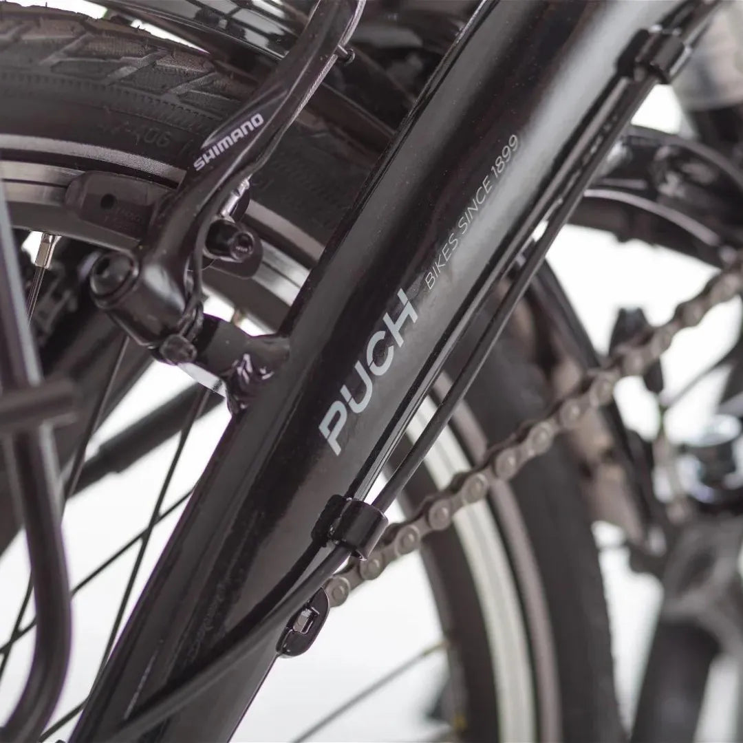 Od blizu posnet črn okvir električnega kolesa Puch H 1 1 z vidno verigo in komponentami Shimano.